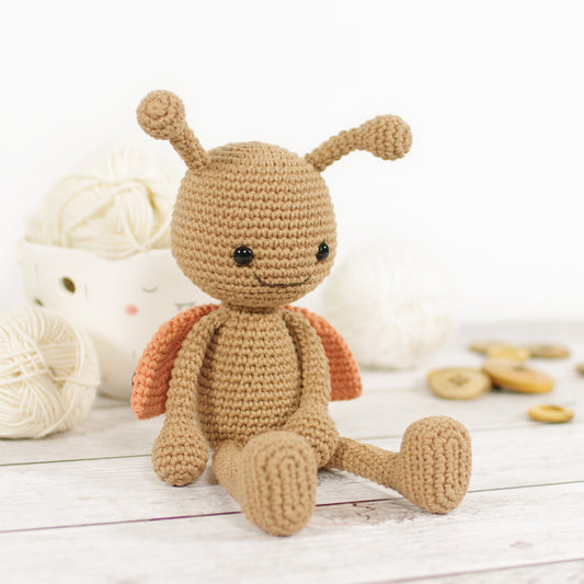 Crocheted toy ladybug on a wooden surface with yarn balls and wooden buttons in the background