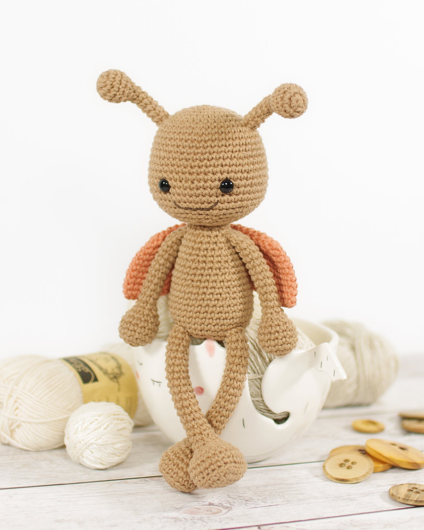 Crocheted amigurumi style ladybug toy on a wooden surface with yarn and buttons.