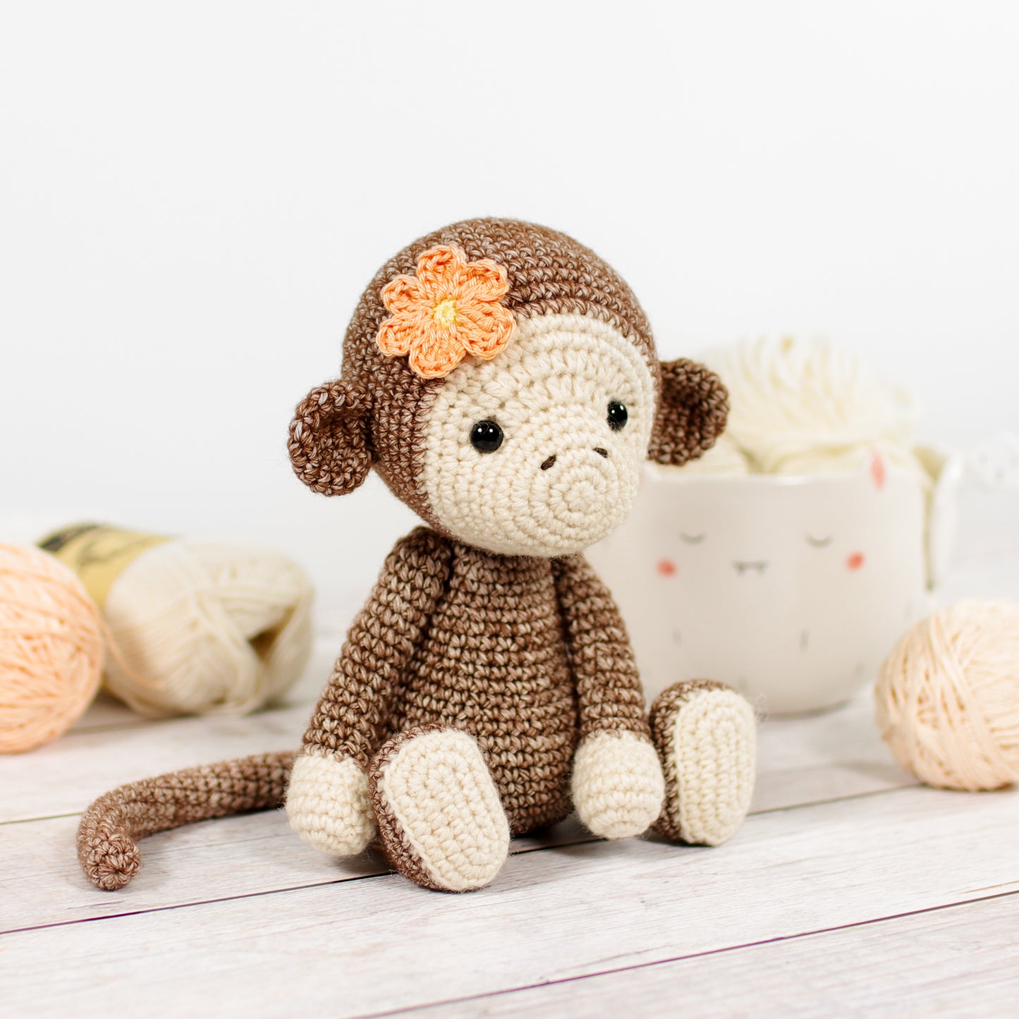 Crochet amigurumi monkey pattern - a brown monkey with a peach-colored flower on its head, sitting next to yarn and crafting materials in the background.