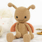 Crocheted toy ladybug with a brown body and orange wings on a light wooden surface.