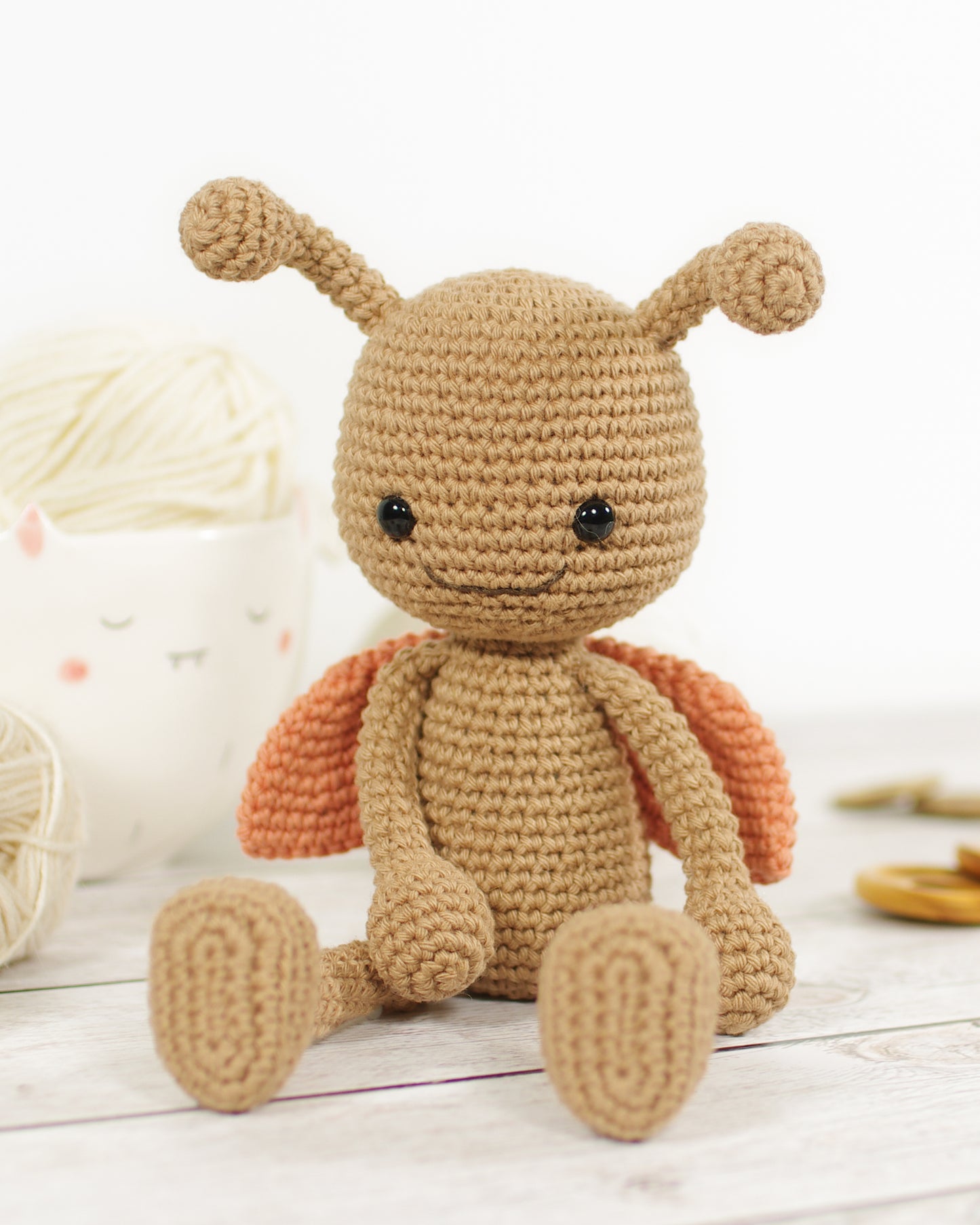 Crocheted toy ladybug with a brown body and orange wings on a light wooden surface.