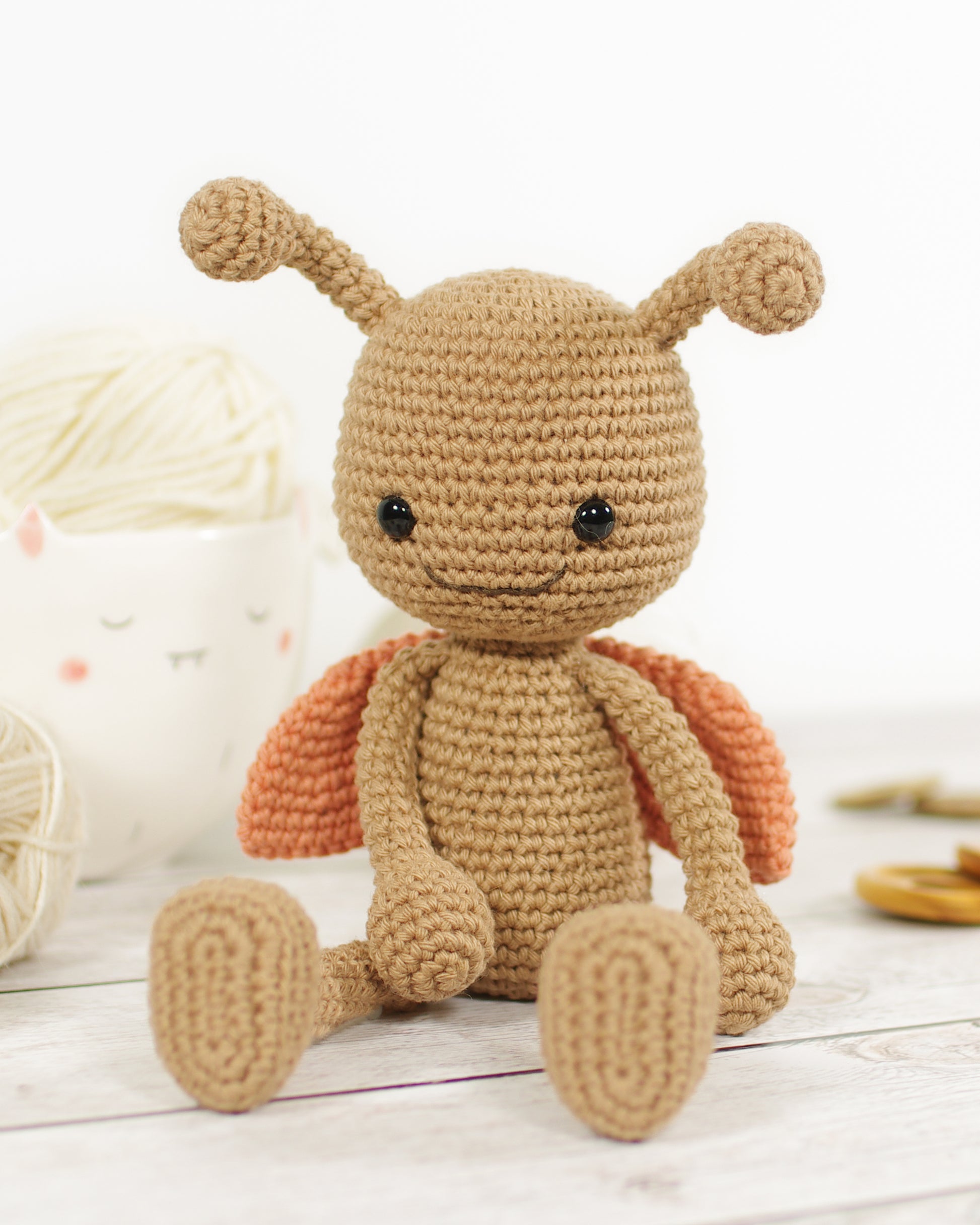 Crocheted toy ladybug with a brown body and orange wings on a light wooden surface.