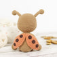 Crocheted ladybug toy on a wooden surface with yarn and crochet hooks in the background.