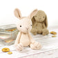 A crocheted amigurumi bunny toy, in beige and brown colors, on a wooden surface, with buttons and yarn nearby.