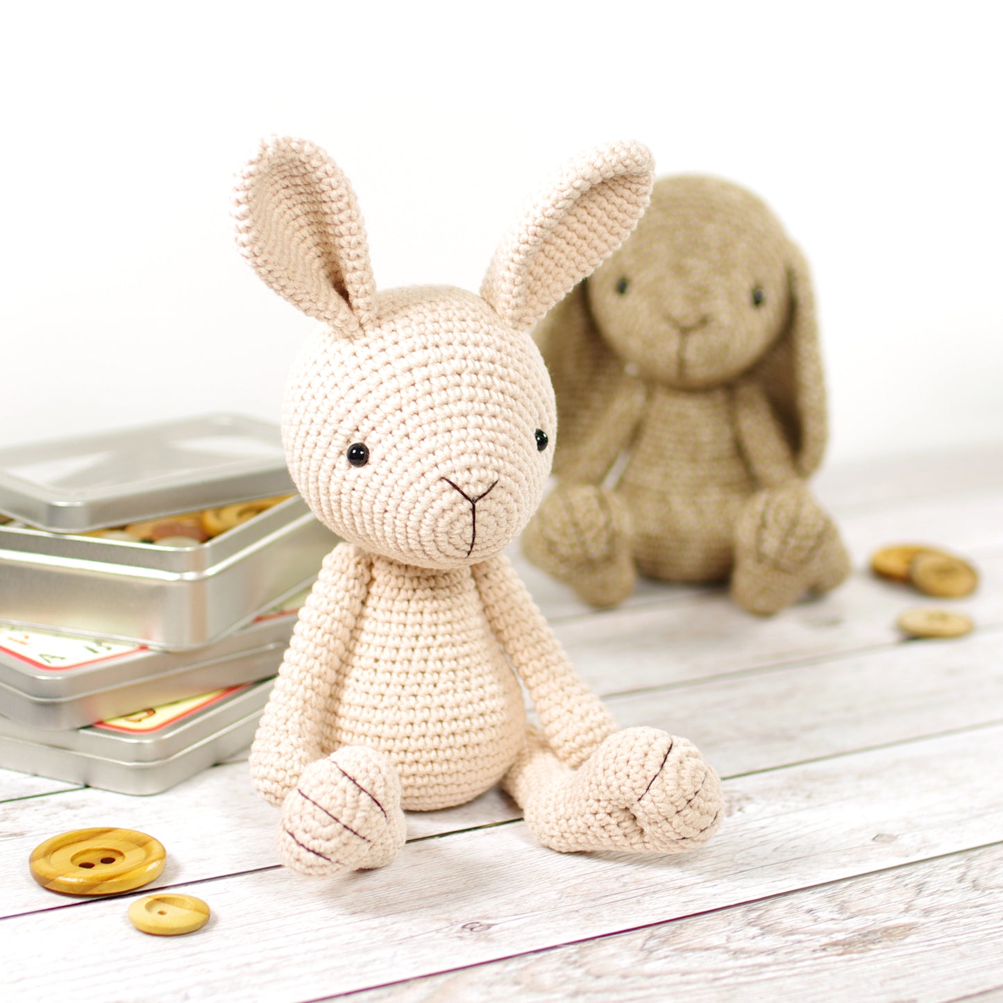 A crocheted amigurumi bunny toy, in beige and brown colors, on a wooden surface, with buttons and yarn nearby.